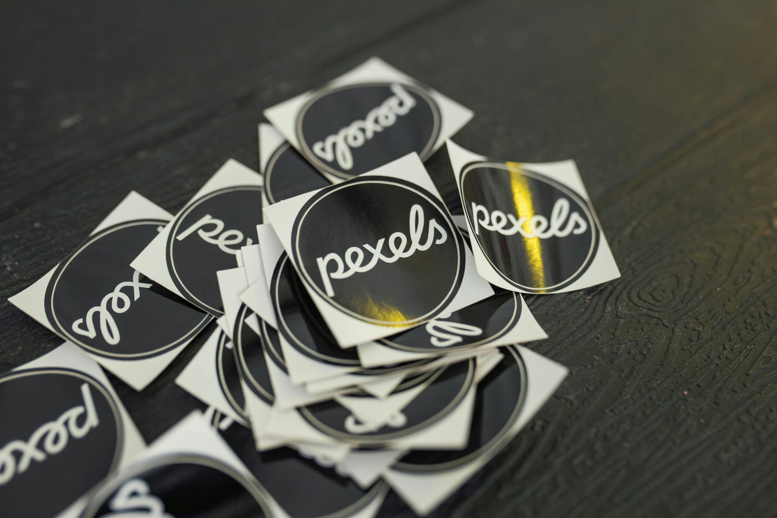 A collection of Pexels branded stickers scattered on a dark wooden surface.